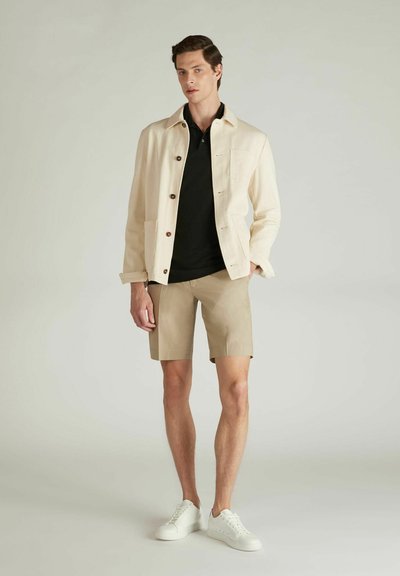 Jasny beżowy żakiet z guzikami, czarna koszulka polo, khakowe szorty i białe trampki. Gładka tkanina, dopasowany krój i minimalistyczny design.