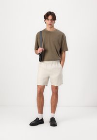 Olivengrønn kortermet skjorte, beige shorts med elastisk liv, svarte sko og grå skulderveske. Minimalistisk stil, ensfargede farger, avslappet passform.