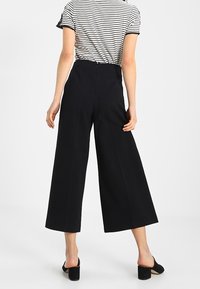 Černé široké kalhoty s vysokým pasem, které mají čisté linie a hladkou texturu, spárované se pruhovaným topem s krátkým rukávem.