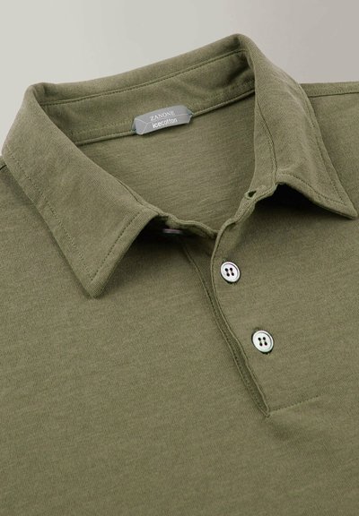 Polo-shirt vert olive en coton doux et texturé, présentant un col classique, une patte de boutonnage à trois boutons et une petite étiquette au niveau du col.