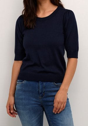 Haut en maille bleu marine avec manches courtes bouffantes, encolure ronde et silhouette ajustée. Le matériau semble doux avec une texture lisse.