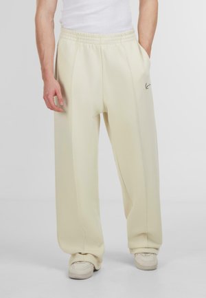 Light cream-colored sweatpants with a relaxed fit, elastic waistband, side pockets, and a small black logo detail on the thigh.