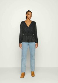 Top preto de manga longa, envolvente, com decote em V, tecido texturizado e cintura franzida, combinado com jeans de perna reta azul clara e botas de tornozelo castanhas.