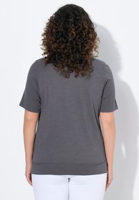 Grijze T-shirt met korte mouwen van lichte stof, met een ronde halslijn en een iets langere achterzoom. Gevoelig met subtiele horizontale lijnen.