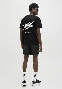 Sort atletisk t-shirt med hvid stjerne grafik på ryggen, parret med sorte shorts, hvide sokker med sort logo og sorte sneakers.