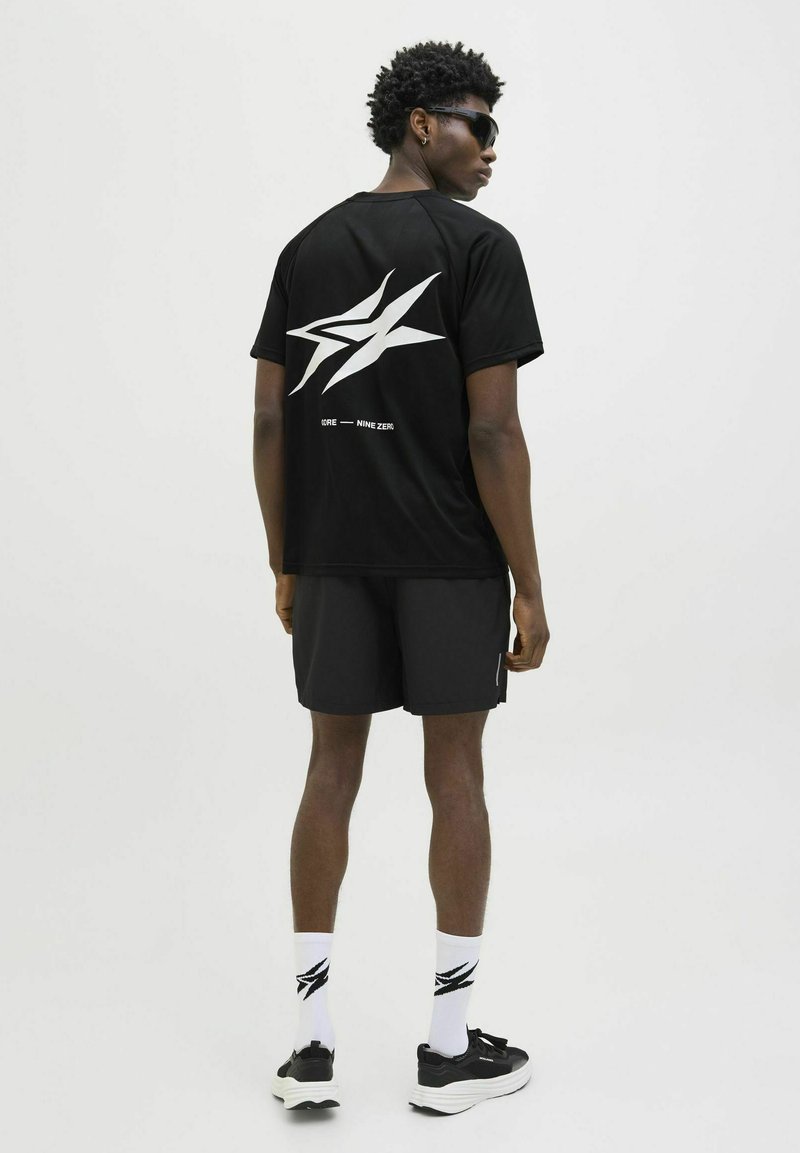 Sort atletisk t-shirt med hvid stjerne grafik på ryggen, parret med sorte shorts, hvide sokker med sort logo og sorte sneakers.