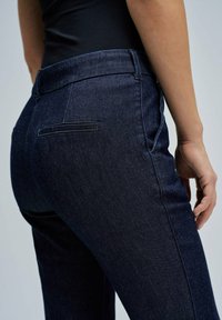 Pantalones de mezclilla azul oscuro de corte slim, con una cintura clásica, un bolsillo trasero y sutiles detalles de costura.