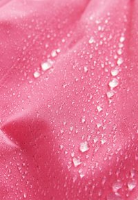 Rosa stof med vanddråber, der perler på overfladen, hvilket viser vandafvisende eller vandtætte materialeteksturer og egenskaber.