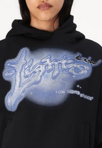 Moletom preto com um estampado gráfico da palavra "Lights" em azul, com um fundo circular azul e um pequeno texto a ler "LOW LIGHTS STUDIOS".