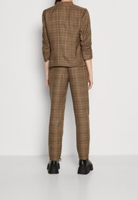 Brun rutig kostym med en figurnära kavaj med trekvartsärmar och raka byxor, kombinerad med klumpiga svarta platåskor.