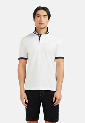 Polo shirt blanc avec un col marine et des poignets de manches marine, comportant une patte de boutonnage à deux boutons et un petit logo sur la poitrine. Les incrustations sont texturées.