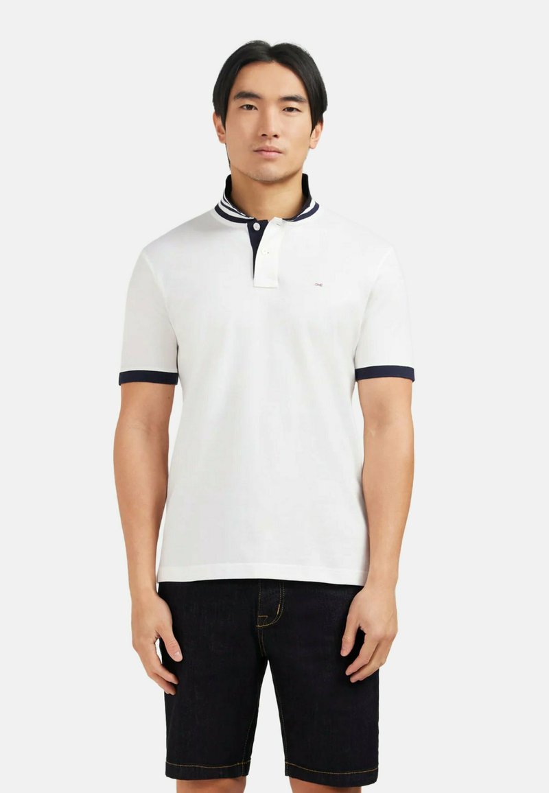 Polo shirt blanc avec un col marine et des poignets de manches marine, comportant une patte de boutonnage à deux boutons et un petit logo sur la poitrine. Les incrustations sont texturées.
