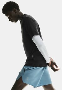 Camiseta negra de manga corta superpuesta sobre una camiseta blanca de manga larga, combinada con pantalones cortos azules que tienen una abertura lateral y un acento de logo.