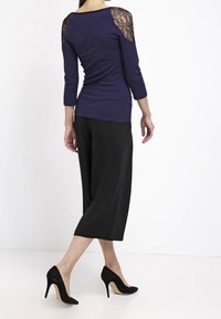 Marineblaues Oberteil mit drei Viertelärmeln und Spitze an den Schultern, kombiniert mit einem schwarzen knielangen Rock und schwarzen High Heels.