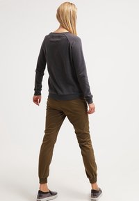 Felpa grigia con una vestibilità rilassata, polsini a costine e collo a giro, abbinata a pantaloni oliva a gamba svasata e sneakers grigie fantasia.