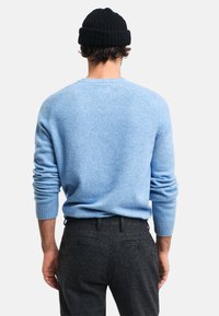 Jasnoniebieski sweter z dzianiny z prążkowanym dekoltem i mankietami, w połączeniu z ciemnoszarymi spodniami z detalami kieszeni. Widok od tyłu.
