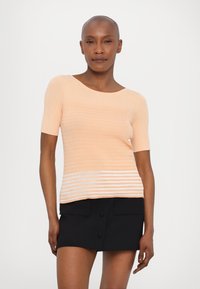 Perzikkleurig gebreid topje met horizontale strepen, ronde halslijn en korte mouwen, gecombineerd met een zwarte hoge taille rok met zakken.