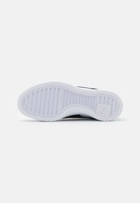 Fekete sneaker talp fehér gumival, bordázott textúrával, vízszintes barázdákkal és egy apró logórészlettel a saroknál.