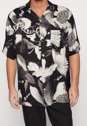 Camicia a maniche corte bianca e nera con motivo floreale astratto audace, indossata con pantaloni neri.