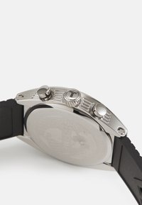Montre en acier inoxydable avec une couronne et des poussoirs texturés, bracelet en caoutchouc noir et un cadran lisse gravé.