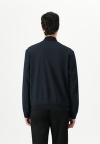 Jachetă de bombardier marinească, cu guler și mansete ribbate, talie elastică și țesătură netedă. Prezintă un design minimalist, fără logo-uri vizibile.