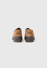 Chaussures en daim marron avec une semelle en caoutchouc noir épaisse. Le design comprend deux accents horizontaux à l'arrière et un talon bas.