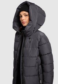 Siva podstavljena jakna s velikim kapuljačom, patentnim zatvaračem sprijeda i bočnim džepovima. Tkanina s teksturom, istaknutim prošivenim uzorkom i crnim detaljima.