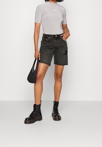 Graues, tailliertes Kurzarmhemd mit "Levi's"-Logo, kombiniert mit schwarzen Denim-Shorts mit fransigem Saum und Seitentasche, abgerundet mit schwarzen Stiefeln.