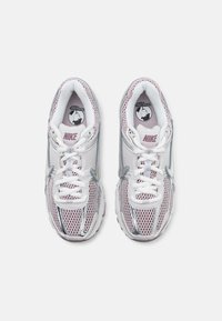 Fehér és világos rózsaszín Nike tornacipők. Háló felsőrész ezüst részletekkel. Fűzők és párnázott gallér a kényelemért. Kör alakú logó a talpbetéten.