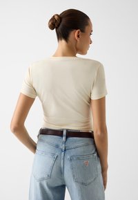 Kremowy dopasowany t-shirt z krótkimi rękawami, połączony z jasnoniebieskimi, wysokim stanem jeansami z czerwonym trójkątnym logo na tylniej kieszeni.