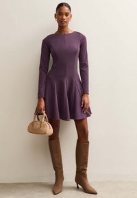 Lila figursydd långärmad klänning med utställd kjol, i kombination med beige knähöga stövlar och en liten beige handväska. Slät tyg med sömdetaljer.