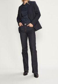 Tummat farkut suoran lahje suunnittelulla, joissa on klassinen viisi-tasku malli ja erottuva tikkaus. Yhdistettynä laivaston siniseen bleiseriin ja paitaan.