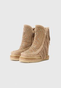 Botas de cuña beige con borlas decorativas, adornadas con embellishements de plata y azul, que cuentan con un suave forro de pelo y cierre de cremallera.