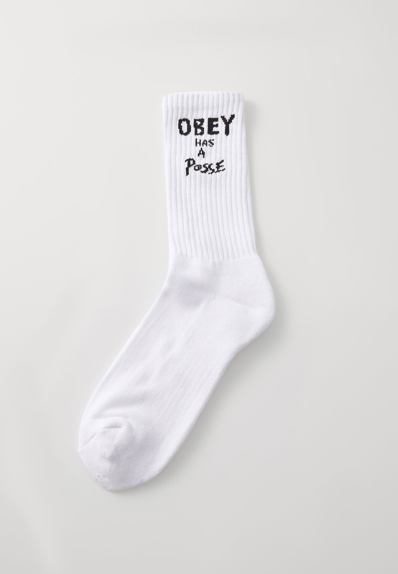 Calcetín de algodón blanco con textura acanalada, que presenta el texto negro "OBEY tiene una pandilla" en la parte superior. Longitud estándar hasta la pantorrilla.