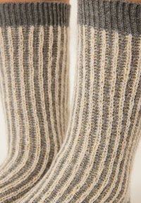 Chaussettes tricotées avec un design côtelé, dans des nuances variées de gris et de crème, agrémentées de fils d'or pour ajouter texture et détails.
