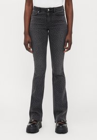 Svarta jeans med utsvängda ben inuti midjan, prydda med små vita nitar utspridda över hela. Robust tyg med lätt stretch.