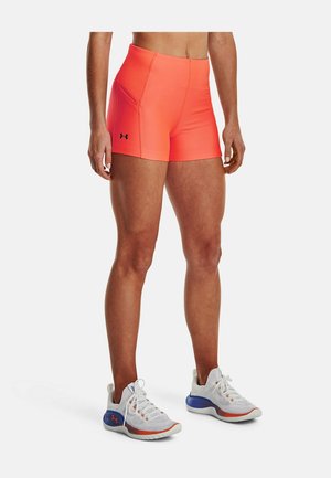 Sportowiec ubrany w neonowo pomarańczowe krótkie spodenki kompresyjne z boczną kieszenią oraz białe buty do biegania z niebieskimi i pomarańczowymi akcentami.