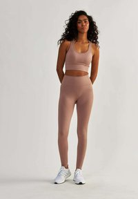 Světlé růžové sportovní set, který obsahuje crop top s ribkovanou texturou a legíny s vysokým pasem a jemným vzorem, doplněné bílými botami.