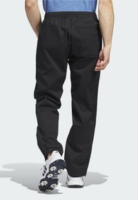 Pantalons de survêtement noirs légers avec une taille élastique et des poignets élastiqués. Dotés d'une poche arrière. Portés avec des chaussures de sport blanches.