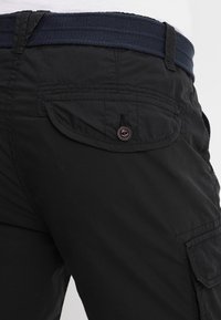 Pantalones cargo negros con un tejido texturizado, un cinturón de lona azul marino y un bolsillo con solapa y cierre de botón en la parte posterior.