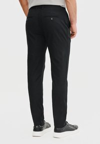 Czarne, dopasowane spodnie wykonane z gładkiego materiału. Posiadają dwie tylne kieszenie zapinane na guziki oraz zwężający się fason nogawek. W zestawie z czarnymi sneakersami.