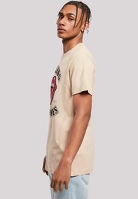 Beige katoenen t-shirt met een graphic van de Rolling Stones. Korte mouwen, ronde hals en een losse pasvorm. Tekst en lippen-logo in rood en zwart.