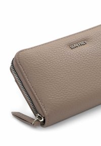 Beige leren portemonnee met een gestructureerd oppervlak, voorzien van een zilveren logo "SURI FREY" en een contrasterende zwarte rits. Compact rechthoekig ontwerp.