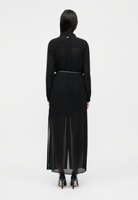 Μαύρο διαφανές μακρύ φόρεμα με μακριά μανίκια, γιακά και σφηκοφωλιά στη μέση με ζώνη αλυσίδα. Λεπτή υφή και μακρύ μέχρι το πάτωμα σχέδιο.