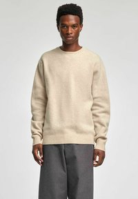 Bēšas krāsas džemperis ar apaļu kakla izgriezumu, ribotiem aprocēm un apakšu. Mīksta tekstūra un brīvs piegriezums. Kombinēts ar pelēkām svītrainām biksēm.