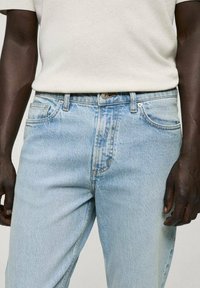 Jeans din denim albastru deschis cu o croială relaxată, design cu cinci buzunare și decolorare ușoară. Prezintă o închidere cu nasture metalic și bucle pentru curea.