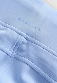 Ljusblå träningsstoff med slät textur och sömnadsdetaljer. Har varumärkeslogotypen "ACTIVE" i en matchande ljusblå nyans.