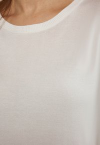 Hvid, bomuldsblandet top med ribbet rund halsudskæring og glat tekstur, med et tætsiddende design og subtil glans.