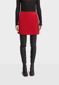 Rode wollen minirok met een aansluitend ontwerp, kenmerkend door strakke lijnen en een gladde textuur, gecombineerd met zwarte leren over-de-knie laarzen.