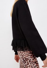 Sudadera negra con un dobladillo rizado texturizado y mangas largas y voluminosas, combinada con leggings estampados que presentan un diseño de leopardo.